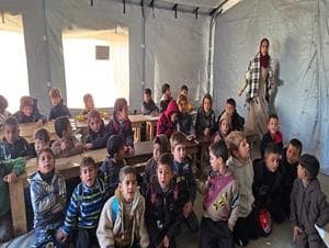 Children seated at desks during a lesson inside an educational tent